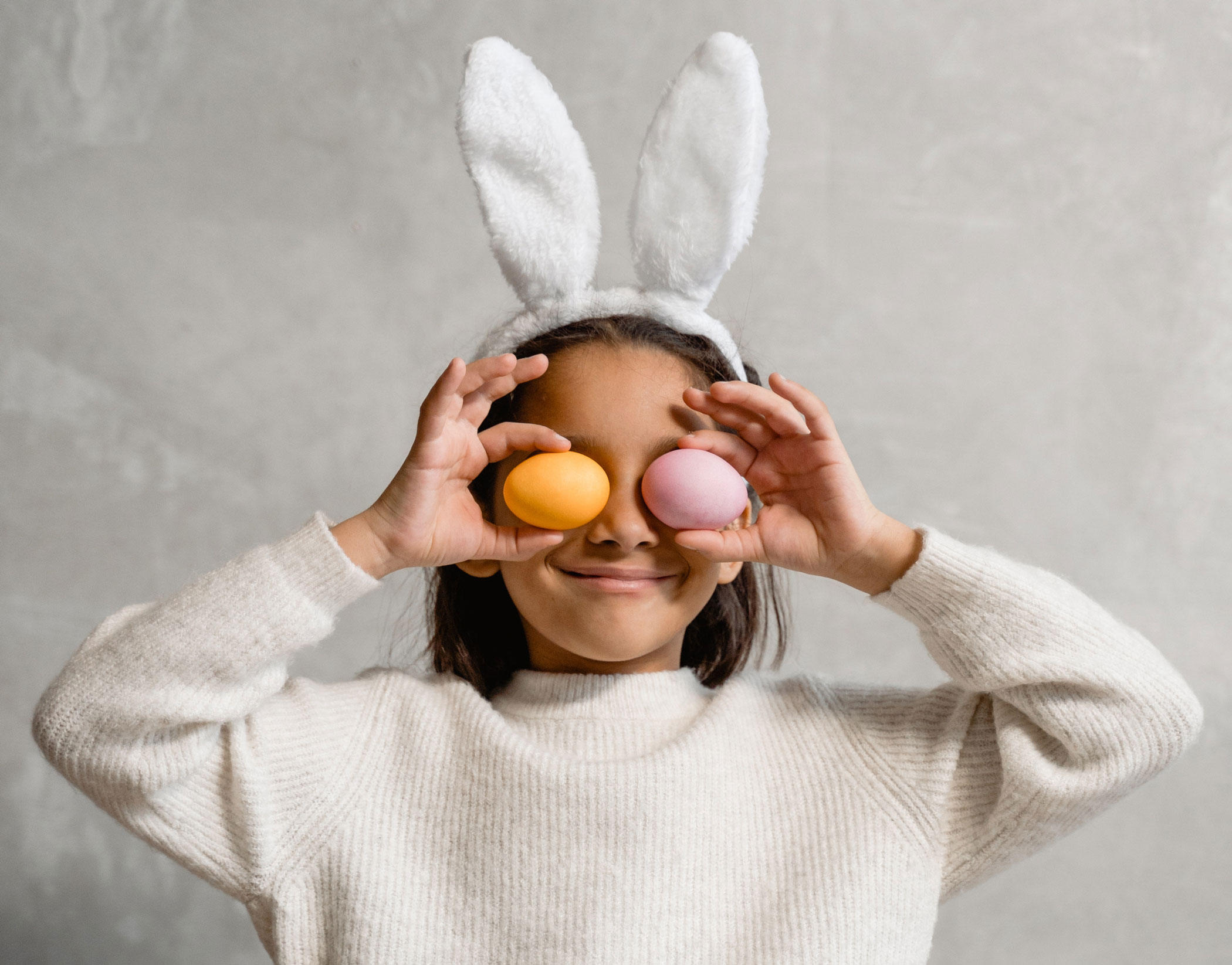 Girl with rabbit ears holding two eggs in front of her eyes